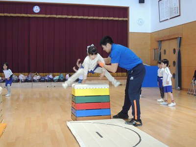 跳び箱を跳ぶ女の子とサポートする講師