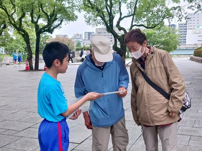 平和記念公園で観光客の夫婦に声をかける児童