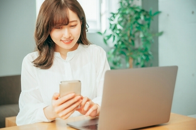 パソコンの前でスマホを操作する女性