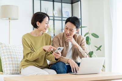 スマホを見ながらリビングで相談する夫婦