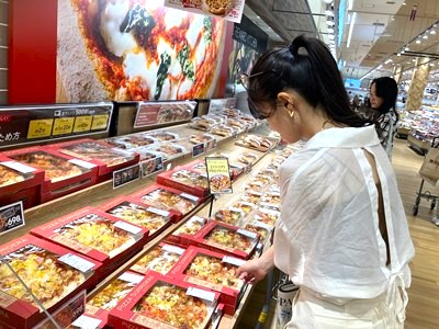 イオンスタイルのお惣菜コーナーでピザを購入する女性