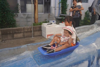氷の滑り台をソリで滑る子ども