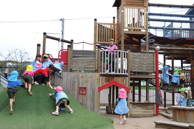 木製遊具と芝生の山で遊ぶ園児