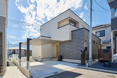 高台に建つベージュとグレーのツートンカラーの家