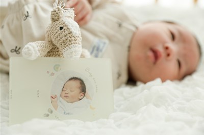 寝ている赤ちゃんの横にある写真入りオリジナルカードと馬の編みぐるみ