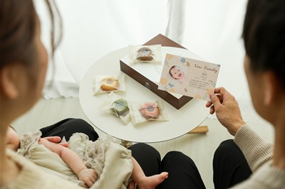 膝に赤ちゃんを抱いている女性と写真入りカードを持っている男性
